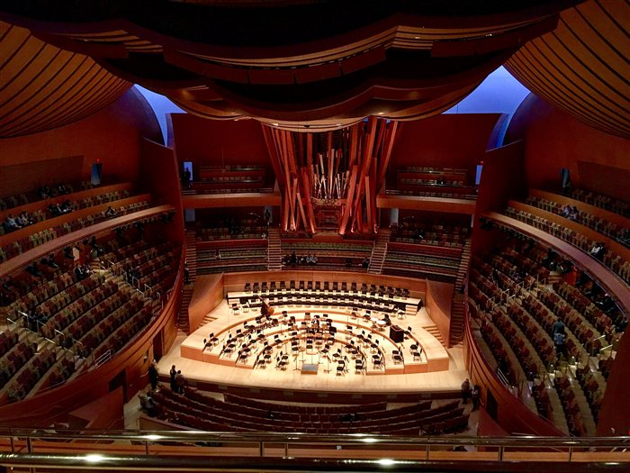 The interior of the Walt Disney Concert Hall in Los Angeles, showing its wavy wood ceiling, pipe organ, and orchestra seating in the round