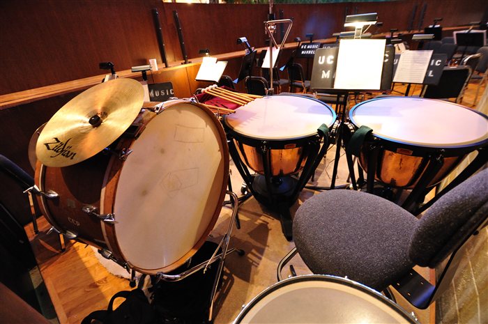 An orchestra pit's percussion setup, showing several copper timpani, a bass drum with an attached cymbal, and mallets laid out ready to play