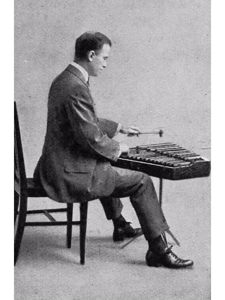 Black-and-white photograph of a seated percussionist striking the metal bars of a glockenspiel with two small mallets